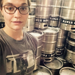 Rose with barrels of beer at the Fair State Brewing Cooperative where she does Quality assurance