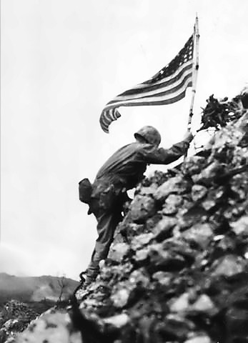 Lt. Col. Richard P. Ross Jr., commander of 3rd Battalion, 1st Marines braves sniper fire to place the United States' colors over the parapets of Shuri Castle on May 30. This flag was first raised over Cape Gloucester and then Peleliu.
