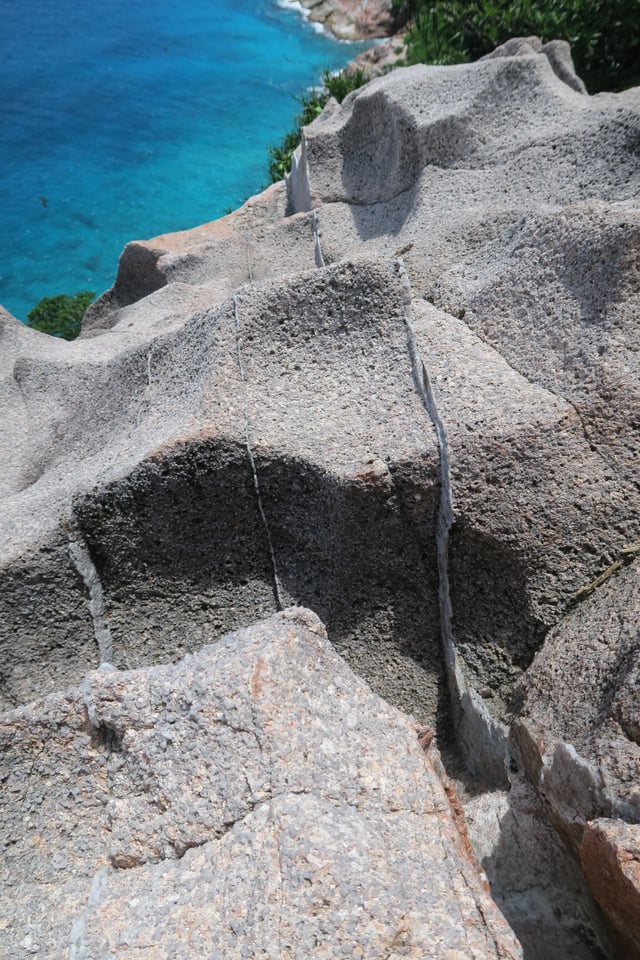 Granite rock in the cliff of Gros la Tête on Aride Island, Seychelles. The thin (1–3 cm wide) brighter layers are quartz veins, formed during the late stages of crystallization of granitic magmas. They are sometimes called "hydrothermal veins".