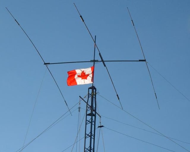 The top of a tower supporting a Yagi-Uda antenna and several wire antennas, along with a Canadian flag