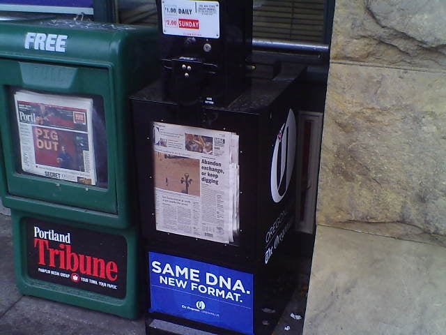 A newly redesigned and installed street vending box for The Oregonian (black) after the paper became a tabloid on April 2, 2014, along with a Portland Tribune box (green)