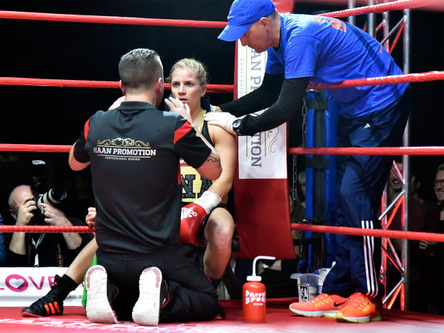 Female boxer Tina Rupprecht receiving instructions from her trainer while being treated by her cutman in the ring corner between rounds.