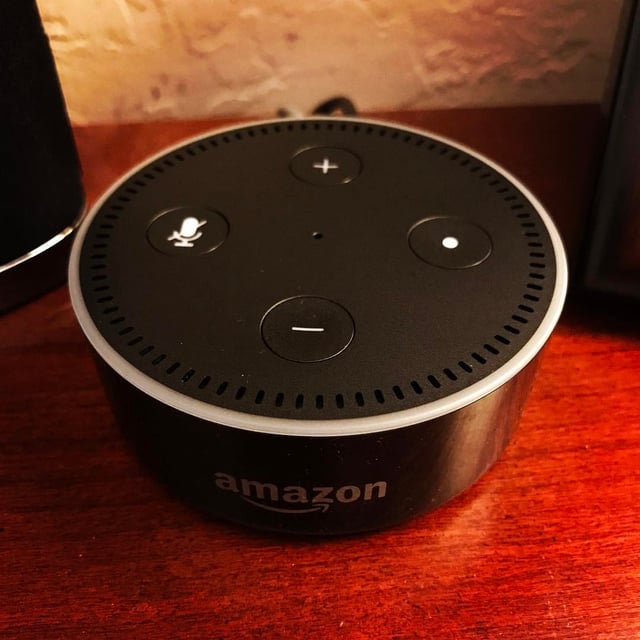 The black Amazon Echo Dot (second generation) sitting idle on a wood surface