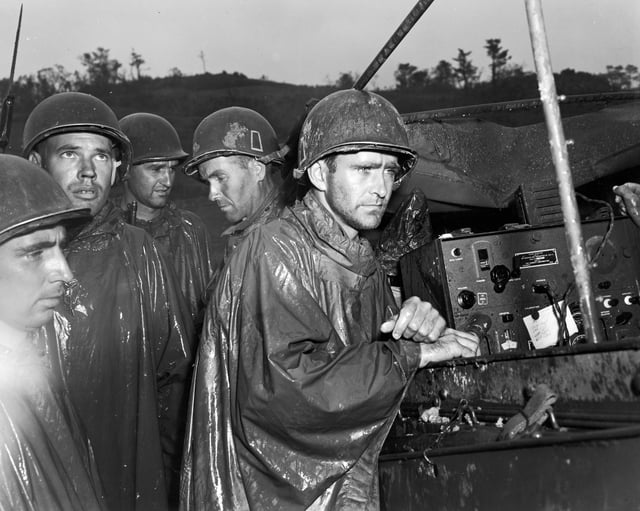 American soldiers of the 77th Infantry Division listen impassively to radio reports of Victory in Europe Day on May 8, 1945.