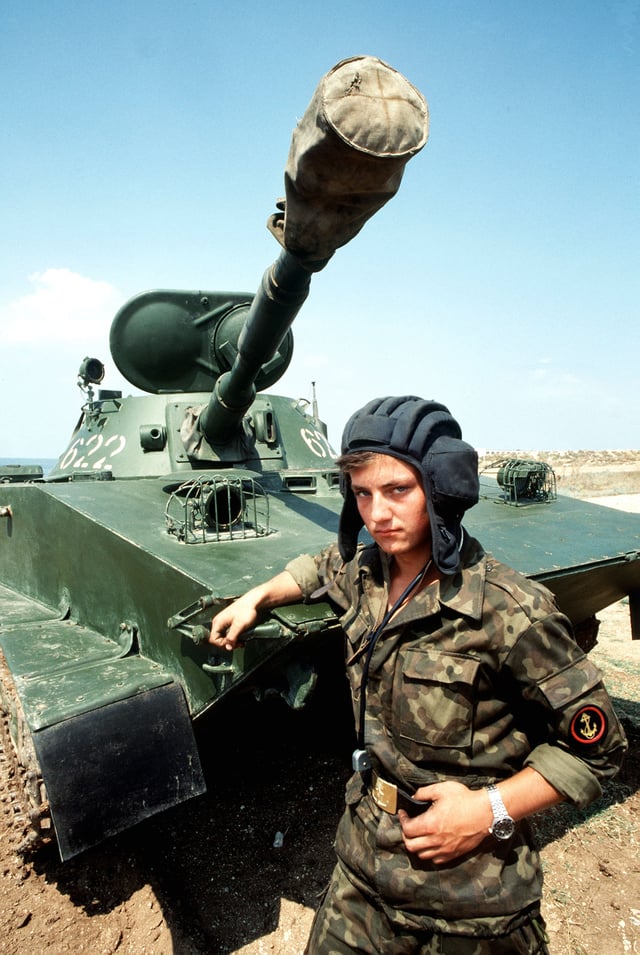 A Soviet naval infantryman stands with his arm rested on his PT-76 amphibious light tank in August 1989. Note the large (opened) oval shaped double hatch, the searchlight on the right hand side of the top of the turret and a radio antenna on the left hand-side of the turret.