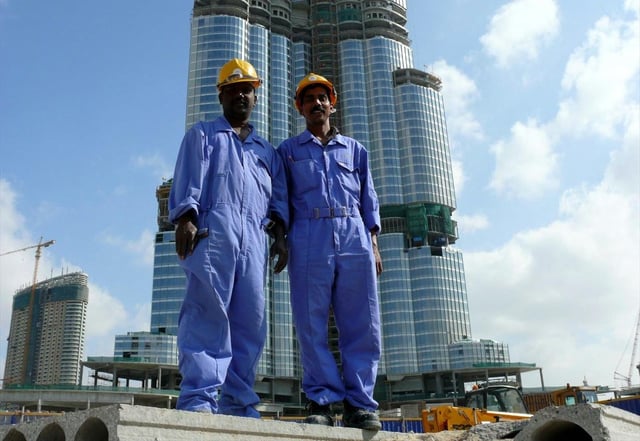 Two south east Asian blue-collar workers posing for a picture with Burj Khalifa on the background.