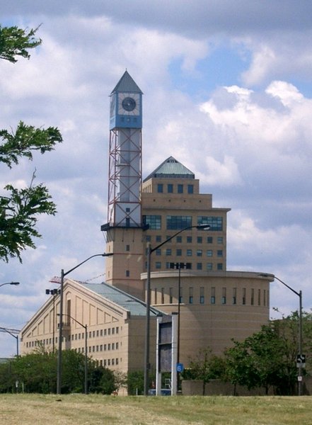 Mississauga Civic Centre seen from the south-east. This design was supposed to reflect the influence of farmsteads which once occupied much of Mississauga, the architecture is based on a "futuristic farm" (the clock tower is the windmill, the main building on the top-right corner is the farmhouse, the cylindrical council chamber is the silo, and the building on the bottom left represents a barn)