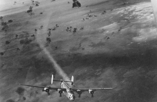 A USAAF B-24 bomber emerges from a cloud of flak with its no. 2 engine smoking.