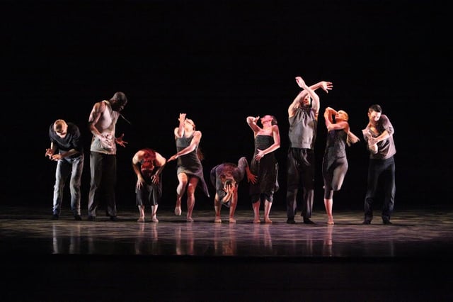 Members of an American jazz dance company perform a formal group routine in a concert dance setting