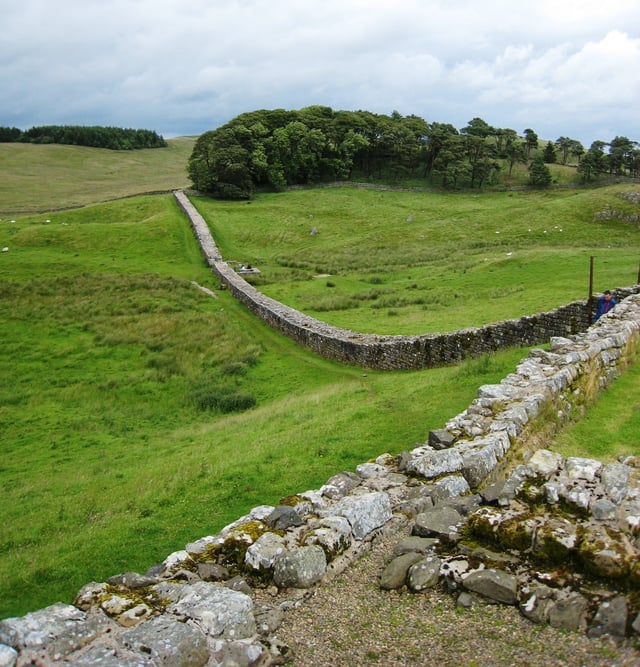 Part of Hadrian's Wall heading east from Housesteads fort, showing the Knag Burn Gateway in the valley. The very flat top of the wall at left is a sign of modern consolidation.