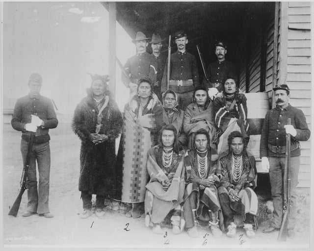 Chief Plenty Coups and seven Crow prisoners under guard at Crow agency. Montana, 1887