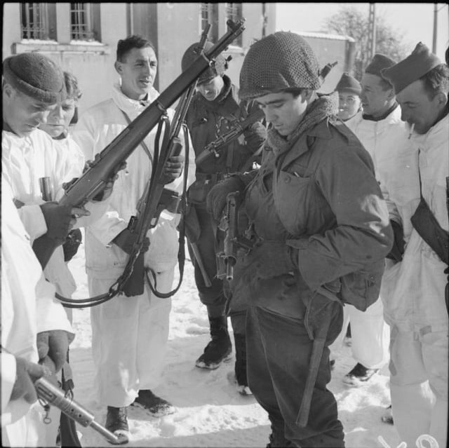 Men from the 5th Battalion, Queen's Own Cameron Highlanders wearing snow suits, inspect the weapons of two GIs from the U.S. 87th Division during the link-up of the two Allied armies at Champlin in Belgium, 14 January 1945.