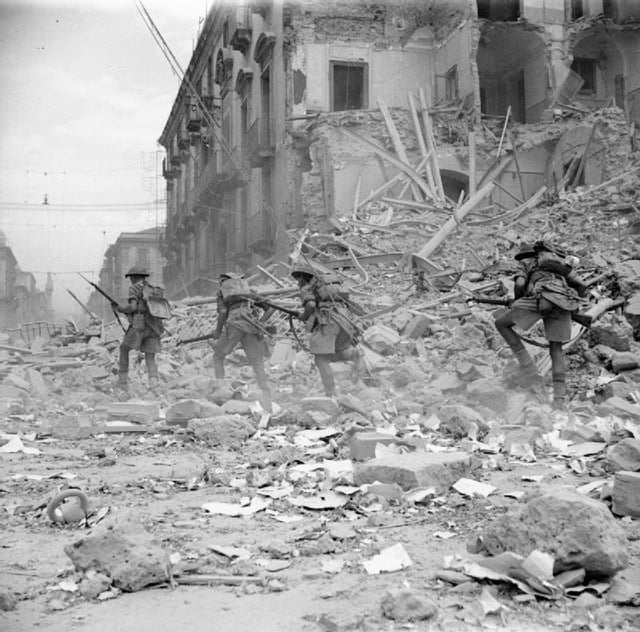 British troops scramble over rubble in a devastated street in Catania, Sicily, 5 August 1943.