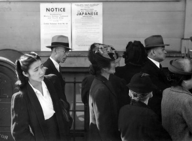 Japanese Americans in front of posters with internment orders