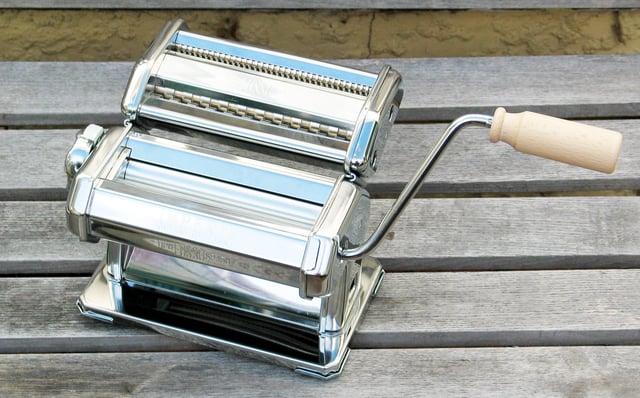 A small hand-cranked pasta machine designed to sheet fresh pasta dough and cut tagliatelle
