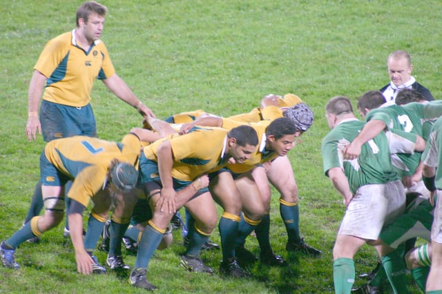 A scrum is preparing to engage. The front row consists of two props on either side of the hooker. The number eight can be seen standing up at the back, while the flankers are bound on the side.