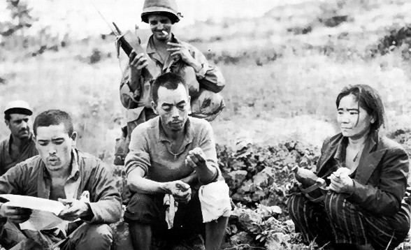 Overcoming the civilian resistance on Okinawa was aided by US propaganda leaflets, one of which is being read by a prisoner awaiting transport.