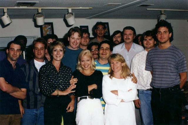 Part of the writing staff of The Simpsons in 1992. Back row, left to right: Mike Mendel, Colin A. B. V. Lewis (partial), Jeff Goldstein, Al Jean (partial), Conan O'Brien, Bill Oakley, Josh Weinstein, Mike Reiss, Ken Tsumura, George Meyer, John Swartzwelder, Jon Vitti (partial), CJ Gibson, and David M. Stern. Front row, left to right: Dee Capelli, Lona Williams, and unknown
