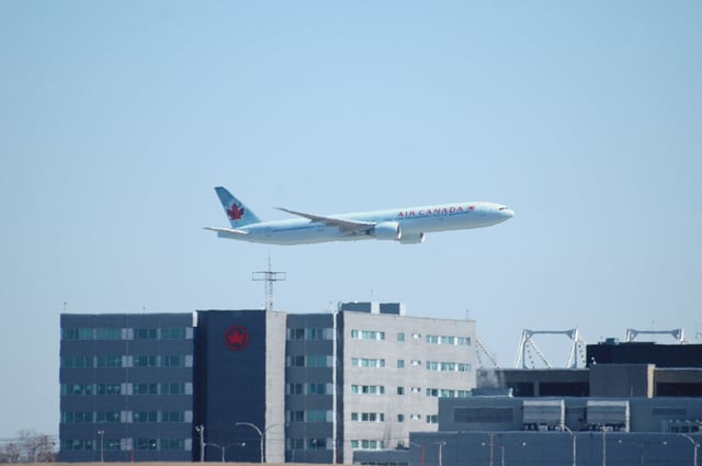 An Air Canada flight flies past the company's corporate headquarters, located at Montréal–Pierre Elliott Trudeau International Airport.