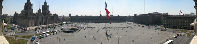 Panoramic view of the Plaza del Zócalo with the National Palace (headquarters of the federal executive branch) in front and flanked by the Metropolitan Cathedral, the Old City Hall and its twin building; both seat of the Government of Mexico City.