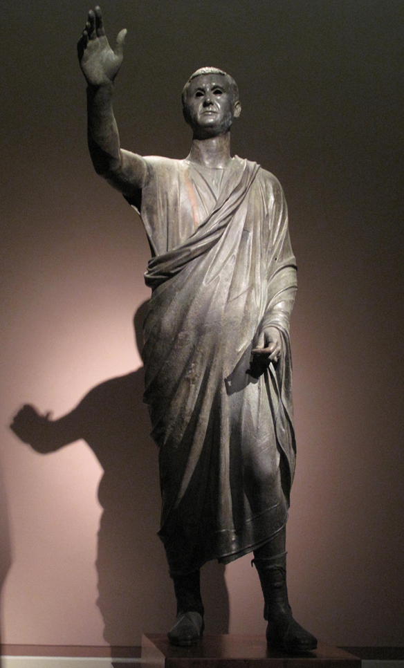 The Orator, c. 100 BC, an Etrusco-Roman statue of a Republican senator, wearing toga praetexta and senatorial shoes; compared to the voluminous, costly, impractical togas of the Imperial era, the Republican-era type is frugal and "skimpy" (exigua).