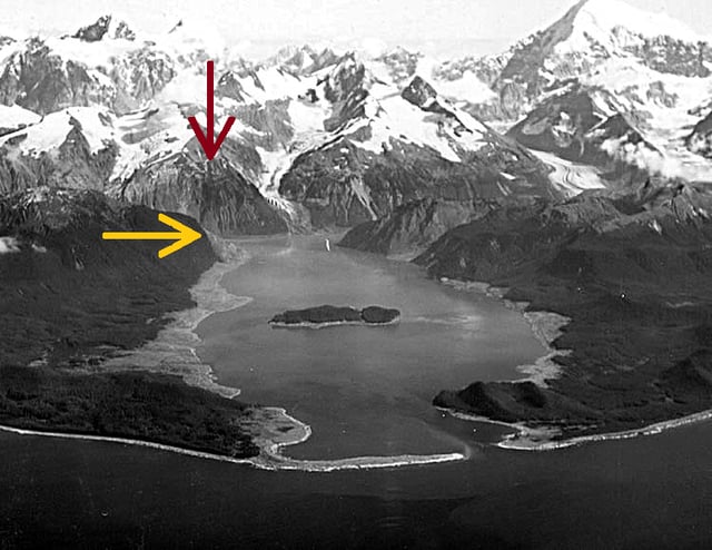 Damage from the 1958 Lituya Bay megatsunami can be seen in this oblique aerial photograph of Lituya Bay, Alaska as the lighter areas at the shore where trees have been stripped away. The red arrow shows the location of the landslide, and the yellow arrow shows the location of the high point of the wave sweeping over the headland.