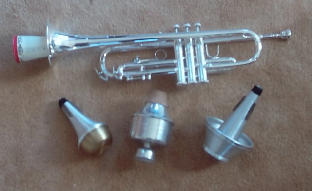 Trumpet with paper straight mute inserted; below are (left to right) straight, wah-wah (Harmon), and cup mutes.