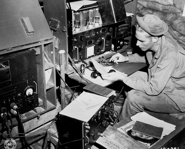 Radio operator Cpl. John Robbins, 41st Signal, 41st Infantry Division, operating his SCR 188 in a sandbagged hut at Station NYU.