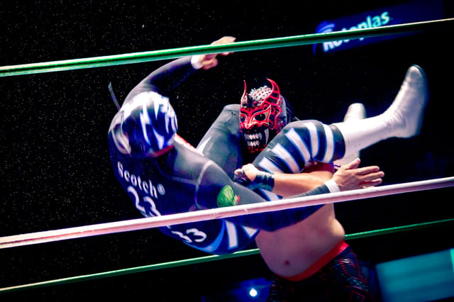 Mexican wrestler La Sombra taking down opponent with a wrestling move
