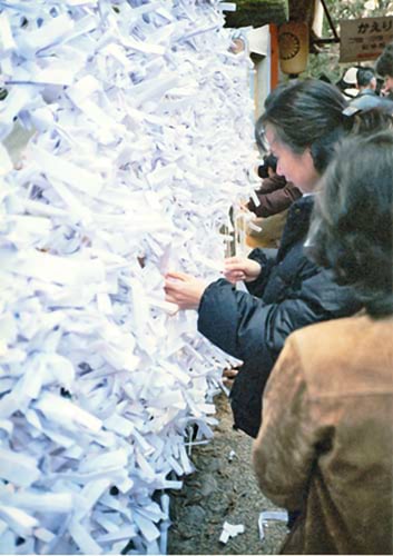 A woman tying her fortune written on a white piece of paper (omikuji) to a frame at Kasuga Shrine