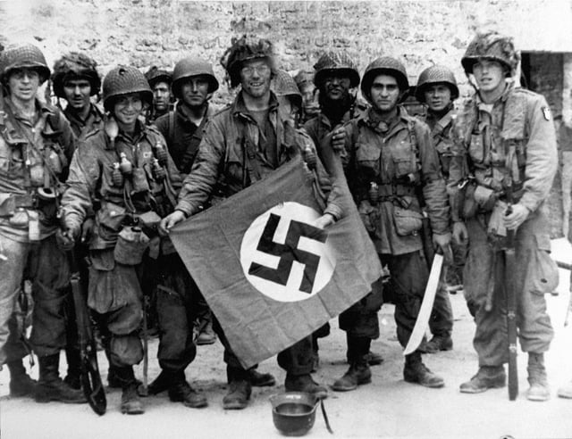 101st Airborne troops posing with a captured Nazi vehicle air identification sign two days after landing at Normandy.