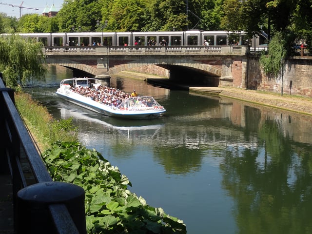 One of Strasbourg's trams passes over one of its canals, whilst a tourist trip boat passes underneath