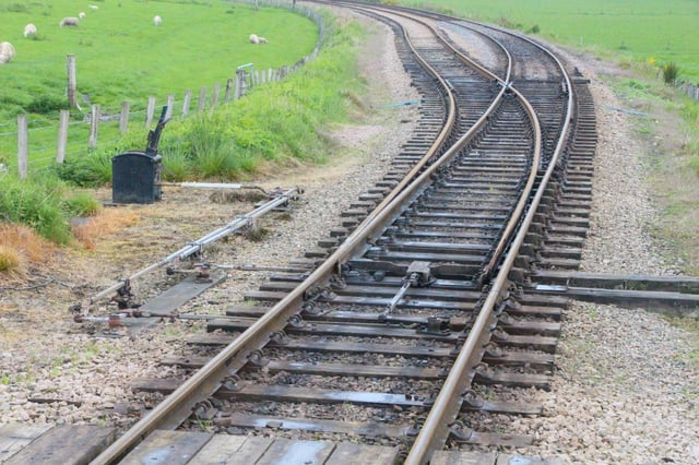 A set of points on the Strathspey Railway in Scotland. The facing point lock in the middle will need to be withdrawn using one of the two levers on the left before the points themselves can be moved using the other lever. Once the points have been moved the lock will be pushed in again to lock the points in position.