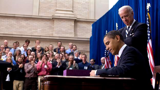 President Barack Obama signs the ARRA into law on February 17, 2009 in Denver, Colorado. Vice President Joe Biden stands behind him.