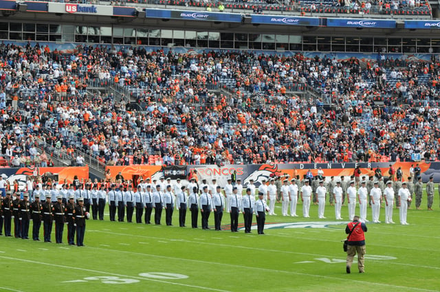 Service members of the U.S. Armed Forces at an American football event: (left to right) U.S. Marine Corps, U.S. Air Force, U.S. Navy and U.S. Army personnel