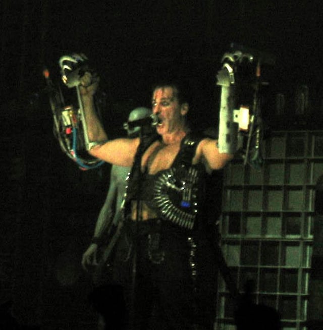 Lindemann during a performance of the song "Rammstein", wearing dual arm-mounted flamethrowers