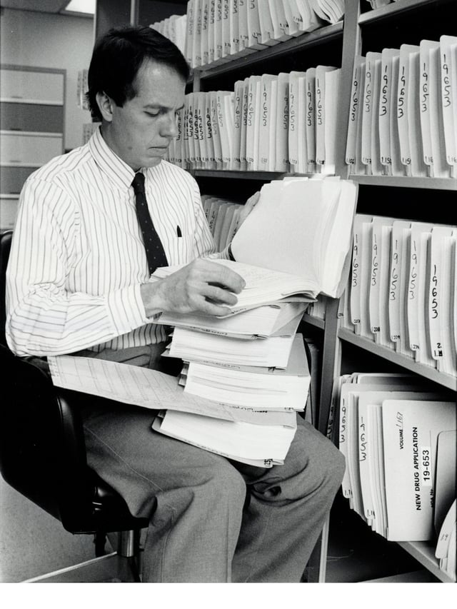 Medical Officer Alexander Fleming, M. D., examines a portion of a 240-volume new drug application around the late 1980s. Applications grew considerably after the efficacy mandate under the 1962 Drug Amendments.