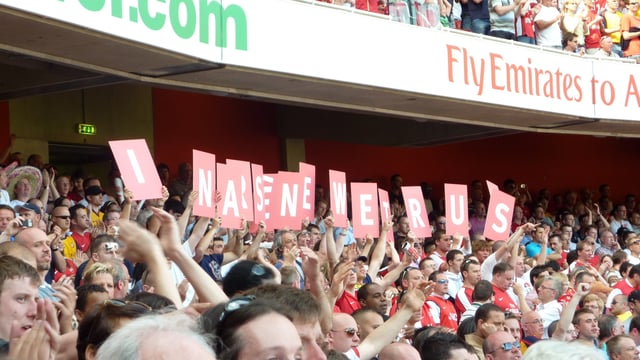 Arsenal supporters hold up cards that spell out "In Arsène we trust"