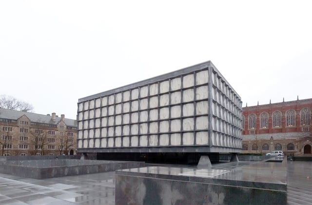 This cloudy day view shows monolithic granite clad piers supporting the building's marble and granite facade. A sunken courtyard, featuring a sculpture designed by Isamu Noguchi is in the foreground at left.