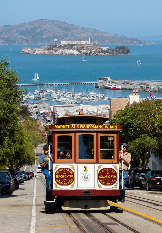 A cable car ascending Hyde St, with Alcatraz on the bay behind