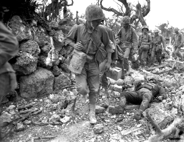 US Marines pass a dead Japanese soldier in a destroyed village, April 1945.