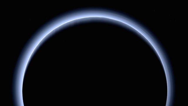 A near-true-color image taken by New Horizons after its flyby. Numerous layers of blue haze float in Pluto's atmosphere. Along and near the limb, mountains and their shadows are visible.