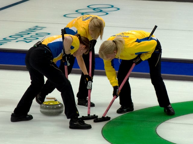 The skip of Team Sweden joins the front end in sweeping a stone into the house at the 2010 Winter Olympics in Vancouver