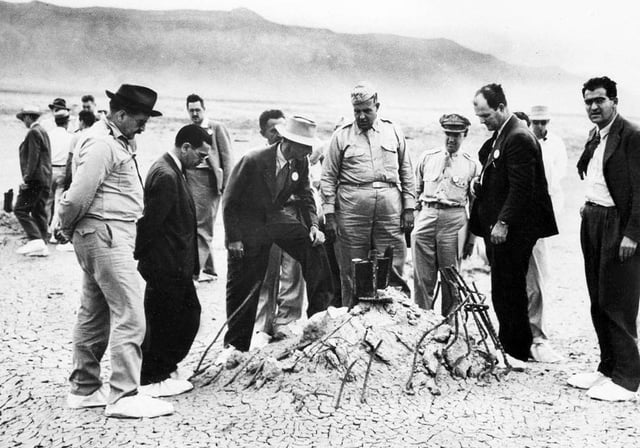 Major General Leslie Groves and Robert Oppenheimer at the Trinity shot tower remains a few weeks later. The white overshoes were to prevent the trinitite fallout from sticking to the soles of their shoes.