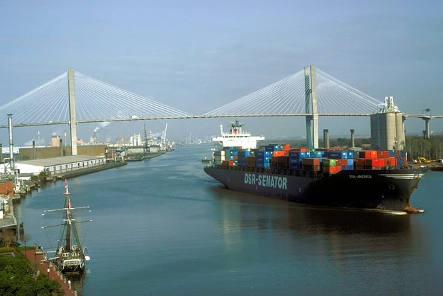 A container ship leaves the Port of Savannah after passing under the Talmadge Memorial Bridge and proceeding down the Savannah River past the Savannah Historic District.