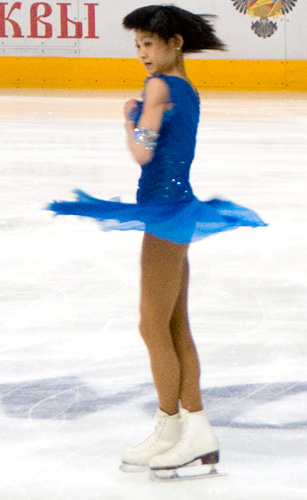 A figure skater conserves angular momentum – her rotational speed increases as her moment of inertia decreases by drawing in her arms and legs.