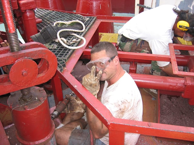 Able seaman using a needlegun scaler on a mooring winch.