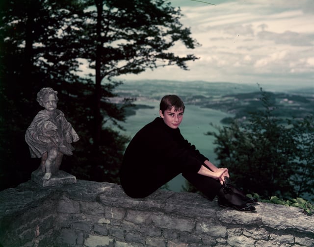 Hepburn with a short hair style and wearing one of her signature looks: black turtleneck, slim black trousers, and ballet flats