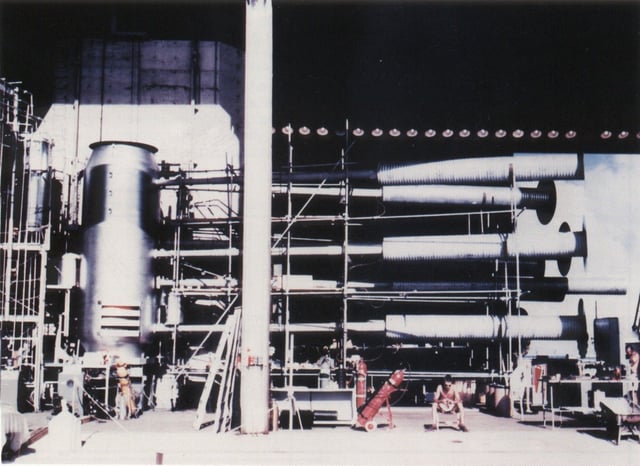 A view of the Sausage device casing of the Ivy Mike hydrogen bomb, with its instrumentation and cryogenic equipment attached. This bomb held a cryogenic Dewar flask containing room for as much as 160 kilograms of liquid deuterium. The bomb was 20 feet tall. Note the seated man at the right of the photo for the scale.