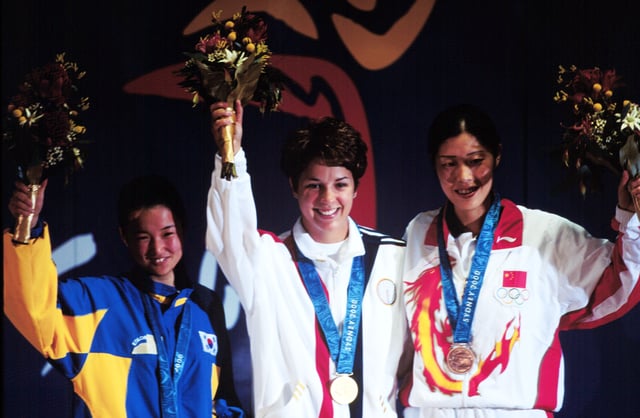 Gold medallist Nancy Johnson (centre) of the U.S., raises her hands with silver medallist Cho-Hyun Kang (left), of South Korea, and bronze winner Gao Jing (right), of China, during the first medal ceremony of the 2000 Olympic Games.